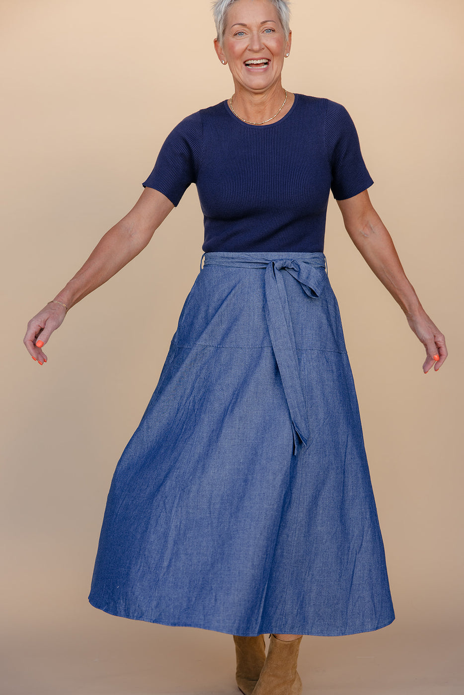 Woman wearing a blue top and denim skirt on a beige background