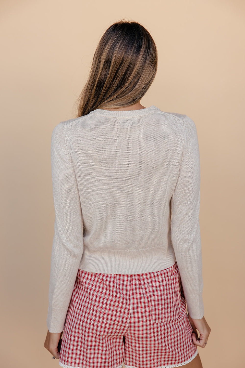 Person wearing a beige sweater and red checkered shorts on a beige background