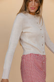Woman wearing a light gray sweater and red checkered pants against a beige background