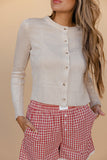 Woman wearing a beige cardigan over a white shirt with red checkered pants on a beige background