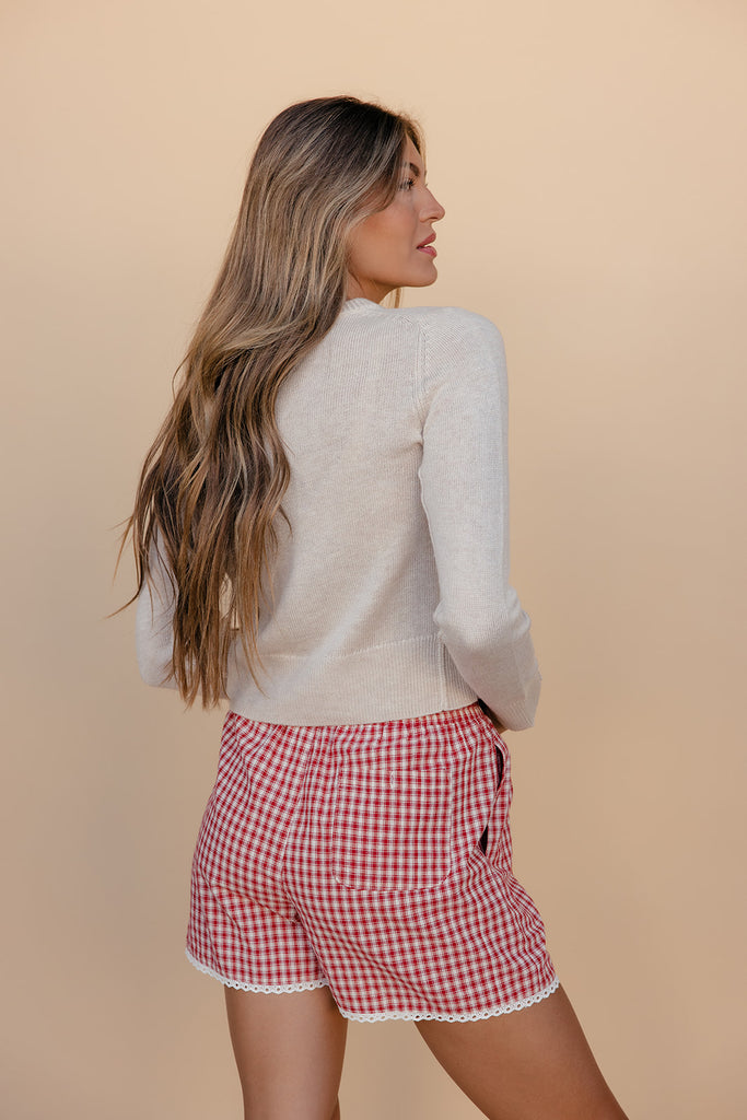 Woman wearing a white sweater and red checkered shorts against a beige background