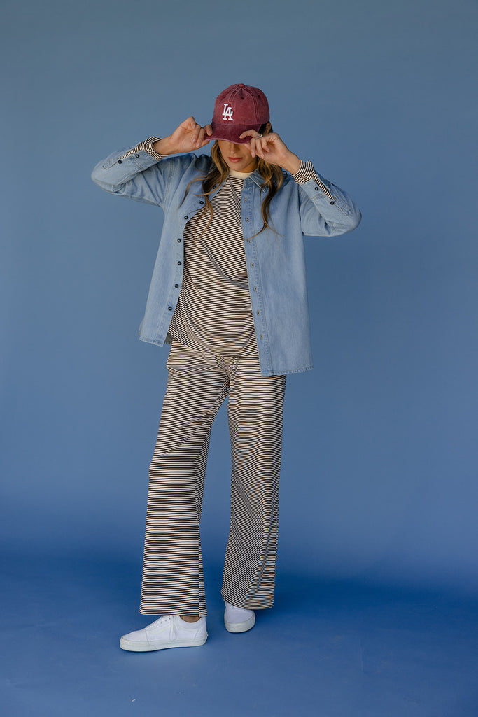 Person wearing a denim jacket, beige shirt, and pants with a maroon cap on a blue background