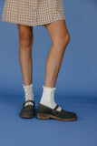 Person wearing a plaid skirt, white socks with lace details, and dark shoes on a blue background