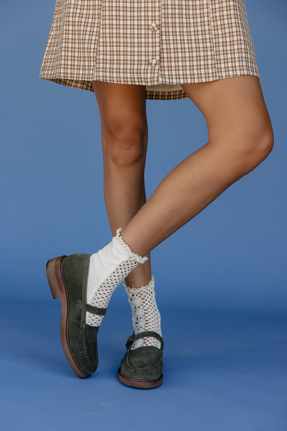 Person wearing a plaid skirt, white socks with black patterns, and green shoes on a blue background