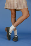 Person wearing a plaid skirt, white socks with black patterns, and green shoes on a blue background