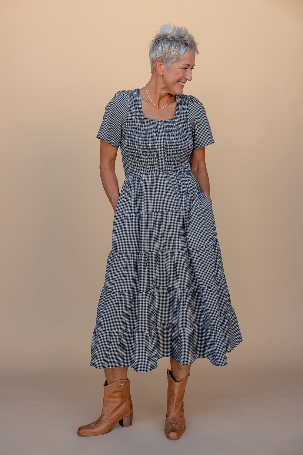 Woman wearing a blue checkered dress with tiered skirt against a beige background