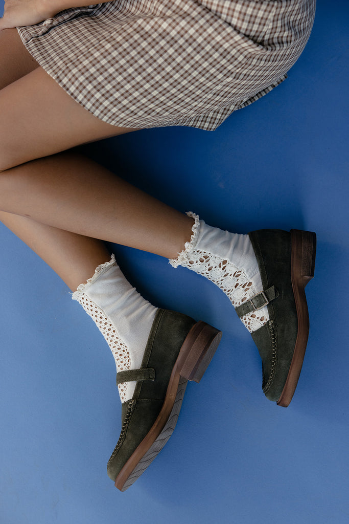 Person wearing green shoes with brown soles and white socks with lace details on a blue background