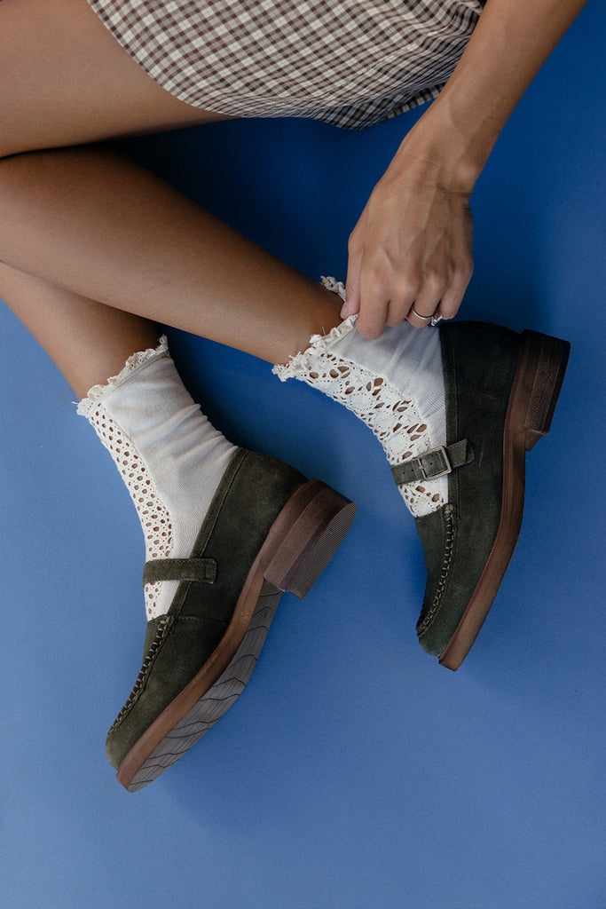 Person wearing green loafers with white socks and lace details on a blue background