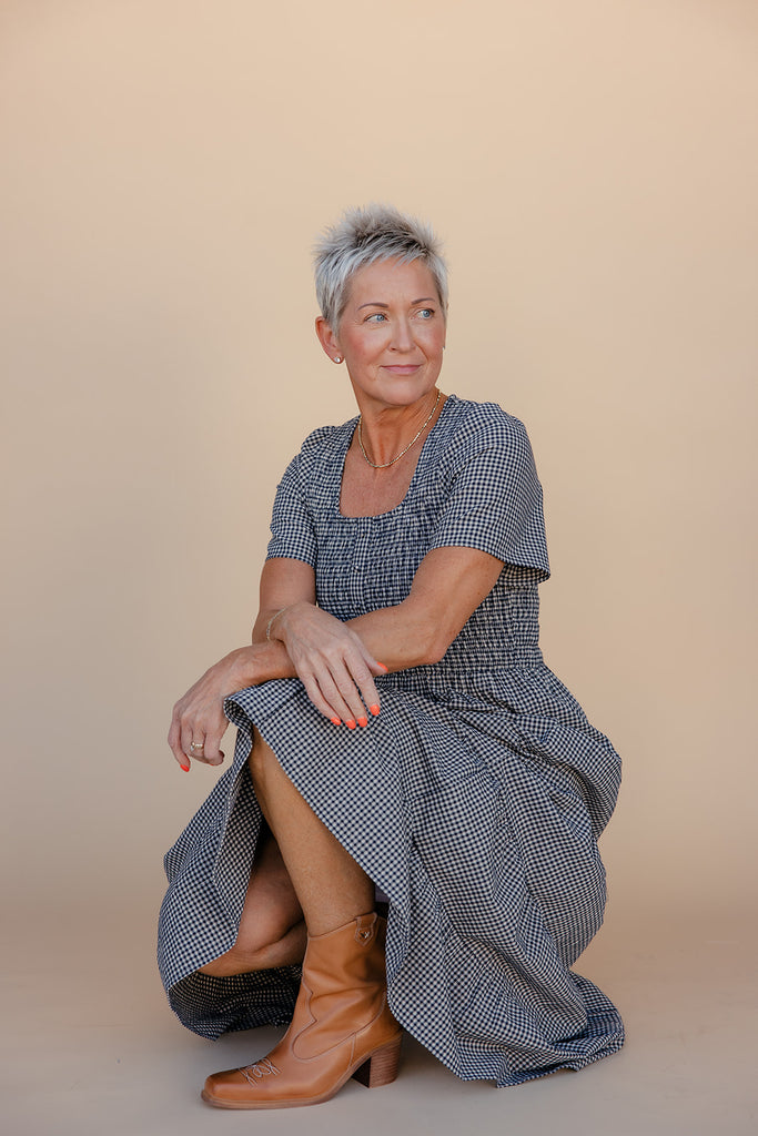 Woman wearing a blue checkered dress sitting on a beige background