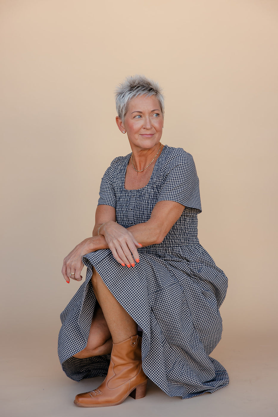 Woman wearing a blue checkered dress sitting on a beige background