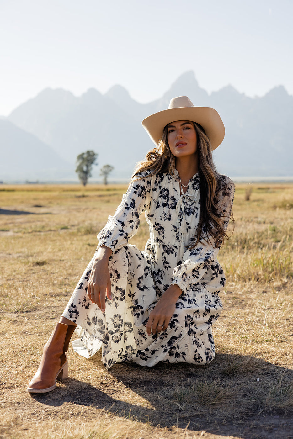 a woman in a white dress and cowboy hat sitting on a field