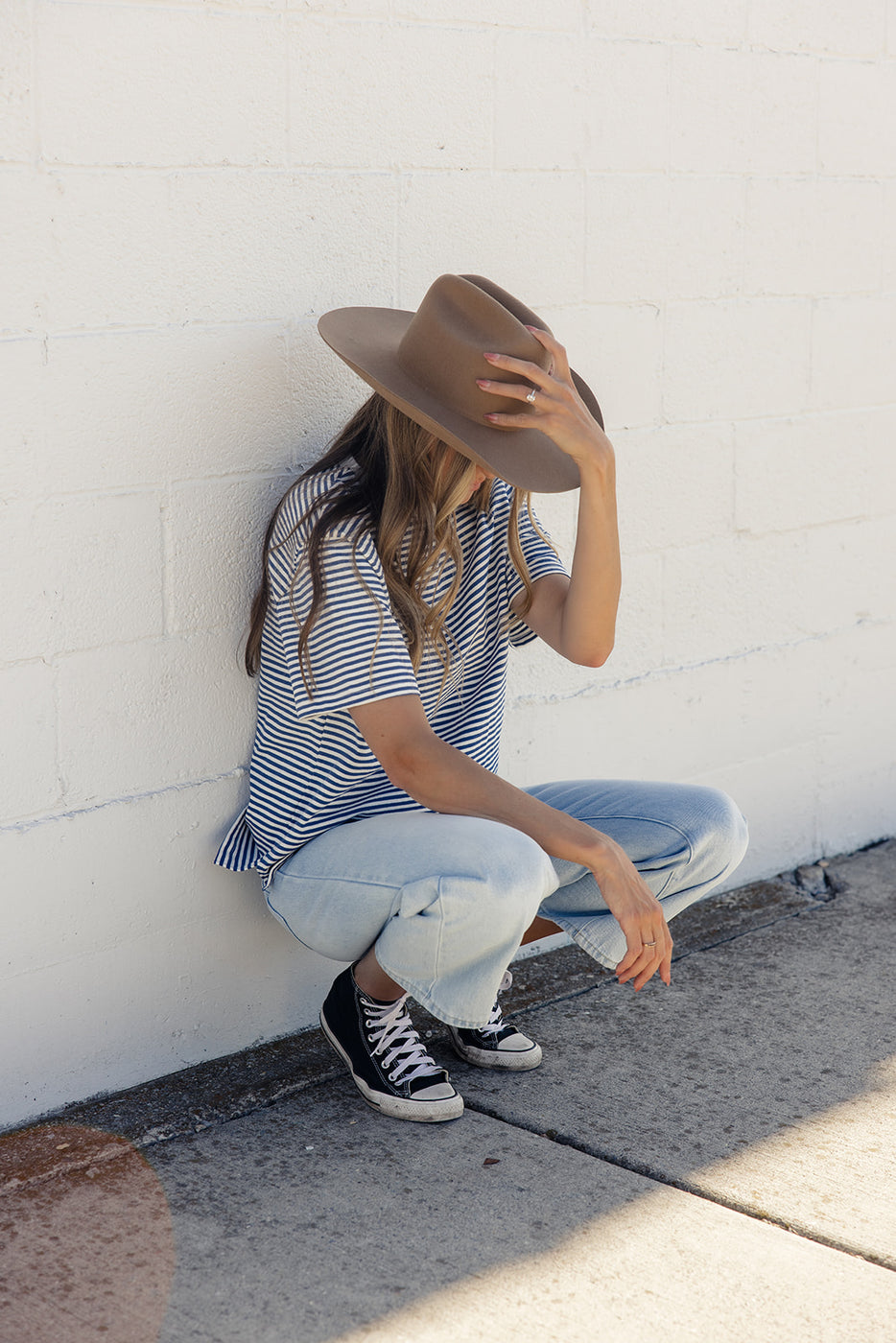 a woman squatting down with her hat over her face