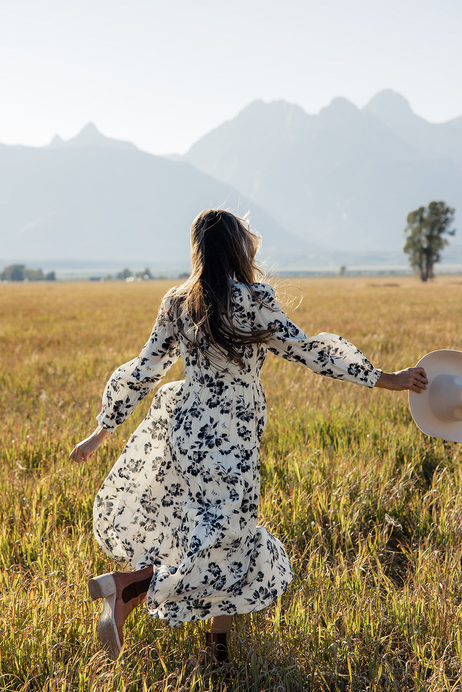 a woman in a dress running through a field with a hat