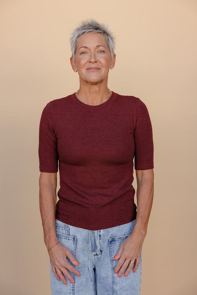 Woman wearing a maroon sweater and blue jeans against a beige background