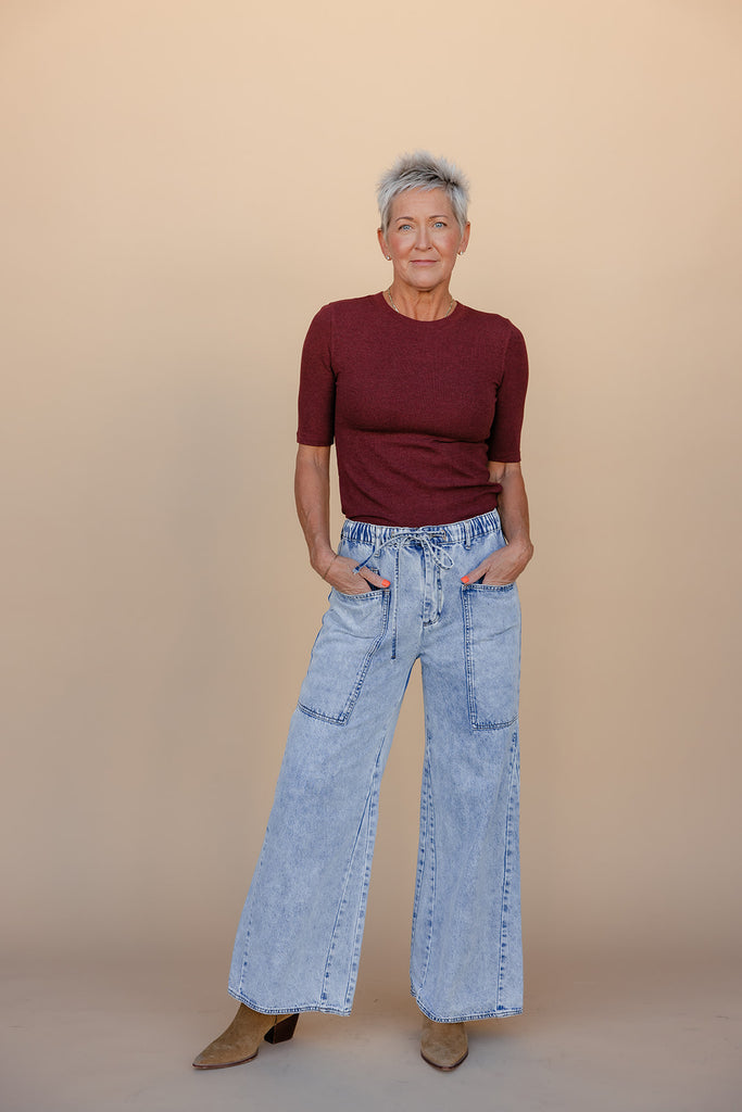 Person wearing a burgundy top and light blue jeans against a beige background