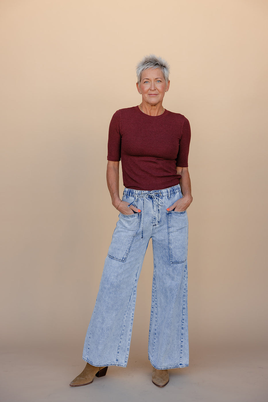 Person wearing a burgundy top and light blue jeans against a beige background