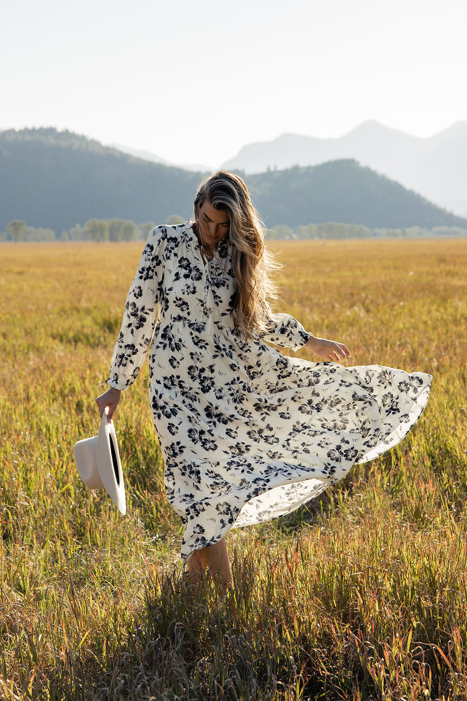 a woman in a long white dress and hat in a field