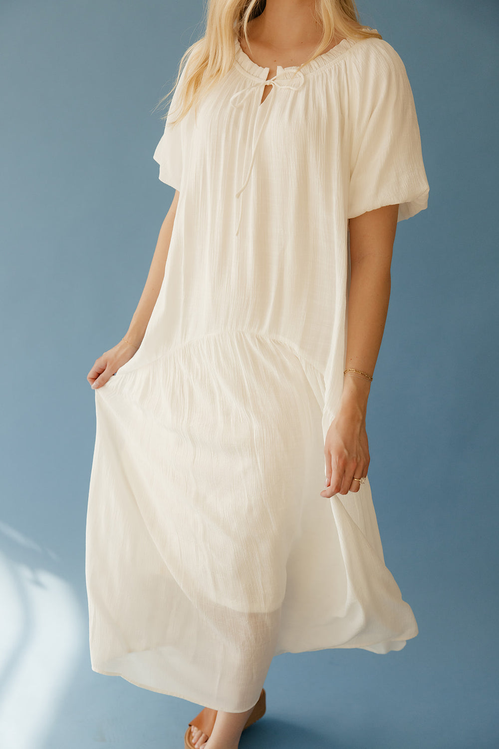 Woman wearing a long, light-colored dress against a blue background