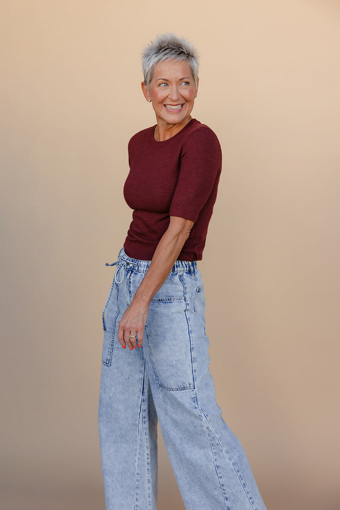 Woman wearing a maroon top and light blue jeans against a beige background