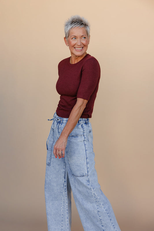 Woman wearing a maroon top and light blue jeans against a beige background