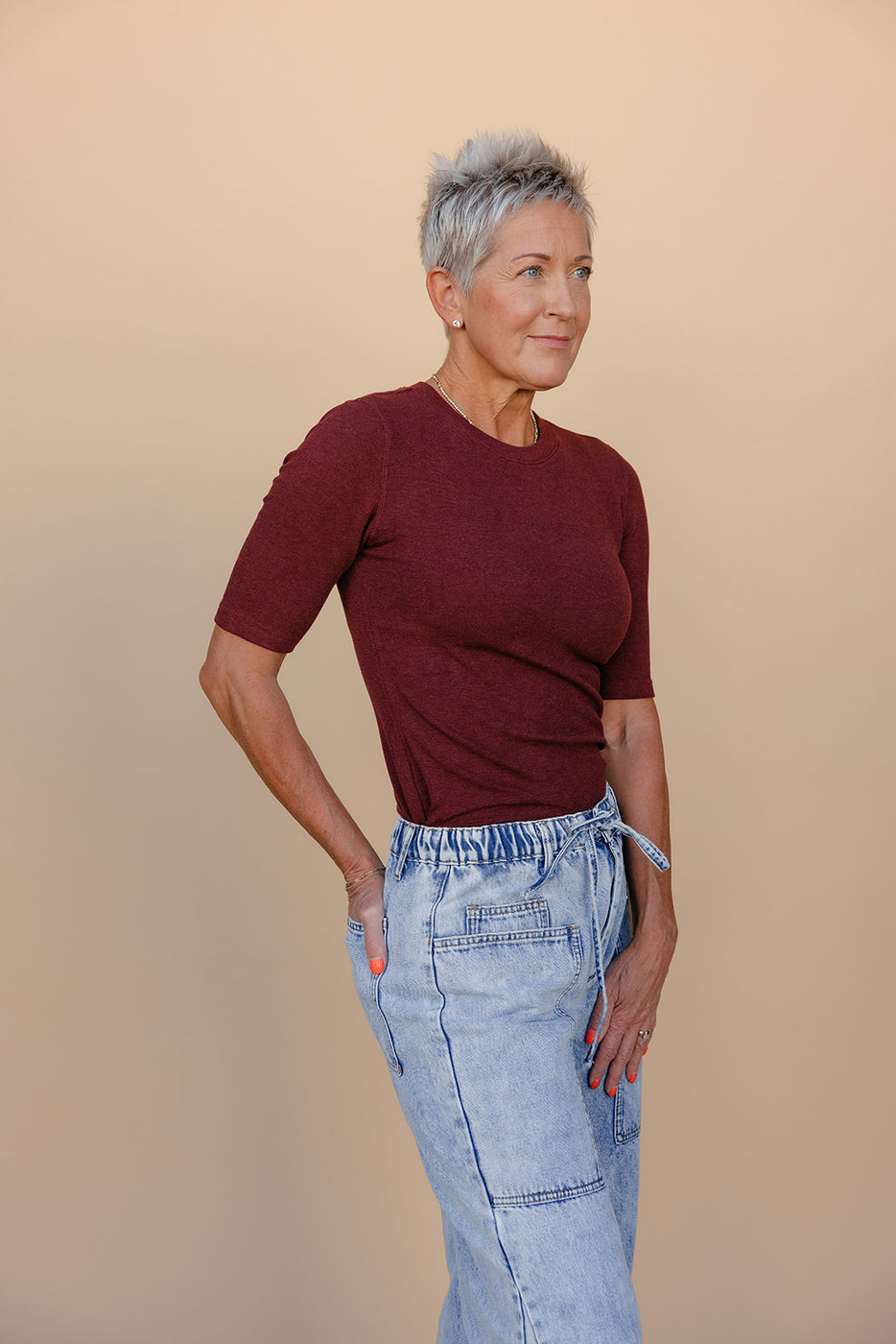 Woman wearing a burgundy top and light blue jeans against a beige background