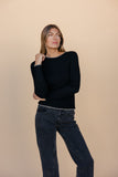 Woman wearing a black sweater and dark jeans against a beige background