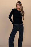 Woman wearing a black sweater and dark jeans against a beige background