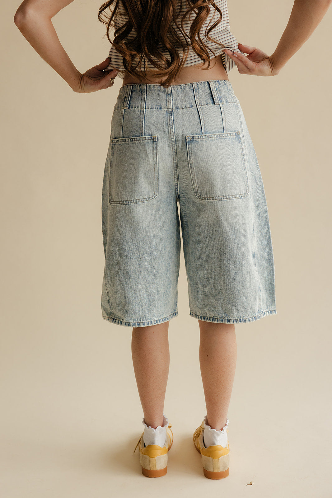 Person wearing light blue denim shorts on a beige background