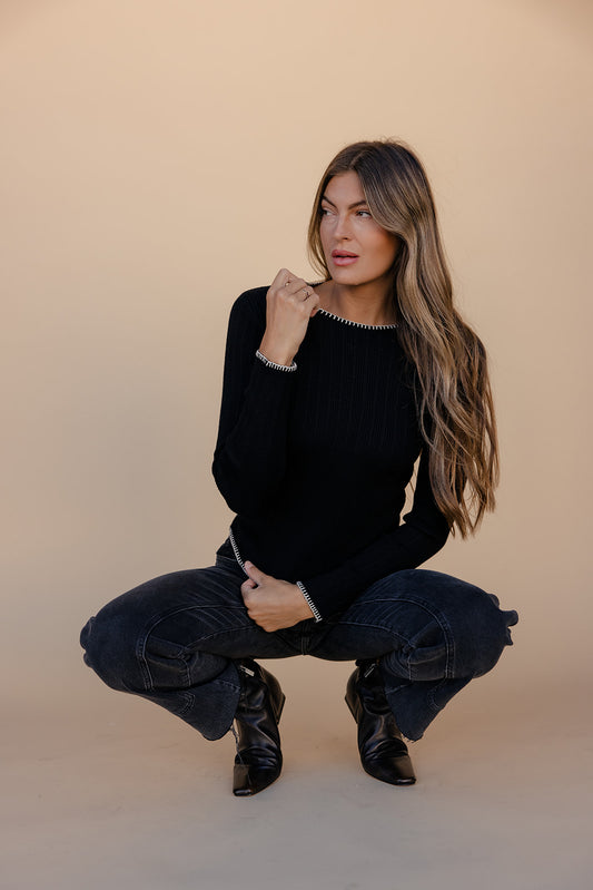 Woman in black sweater and jeans posing against a beige background