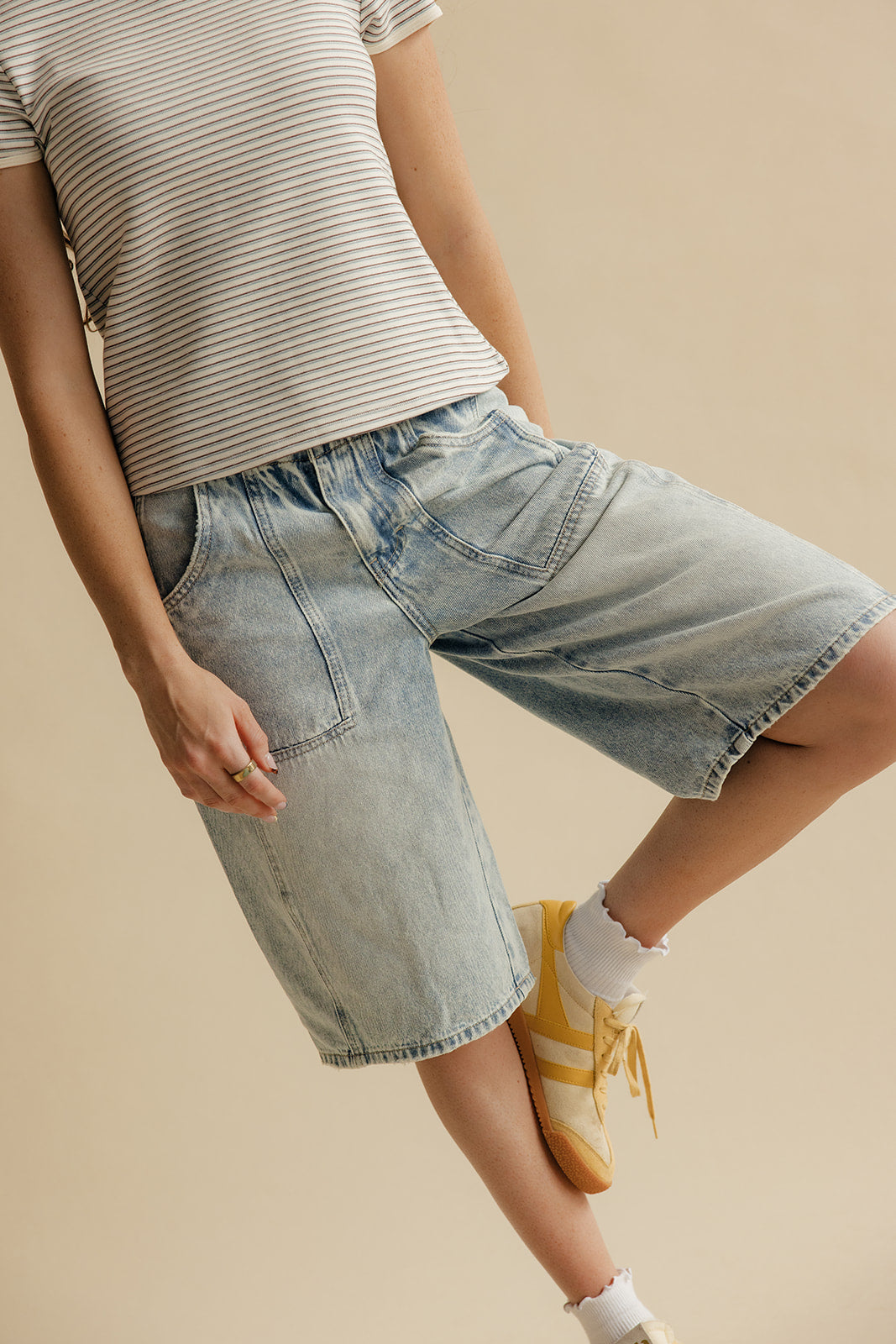 Person wearing a striped shirt and denim shorts on a beige background