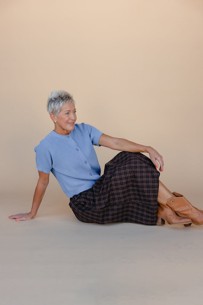 Woman sitting on the floor wearing a blue shirt and plaid skirt with a beige background