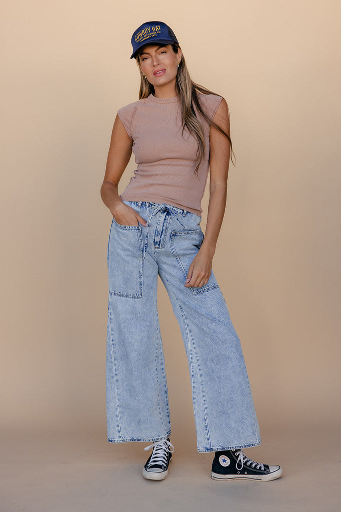 Woman wearing a cap, tank top, and jeans on a beige background