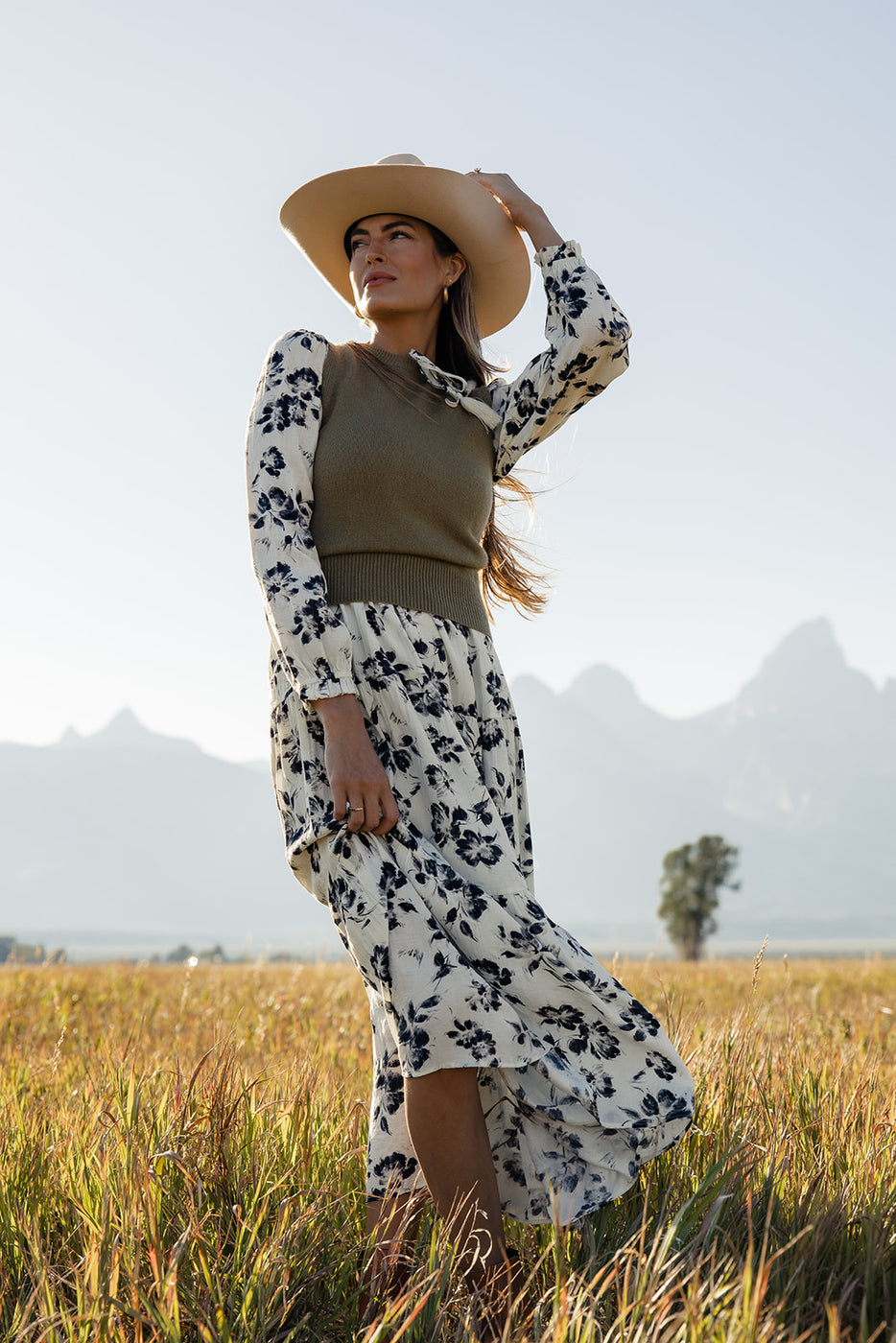 a woman in a long dress and hat in a field