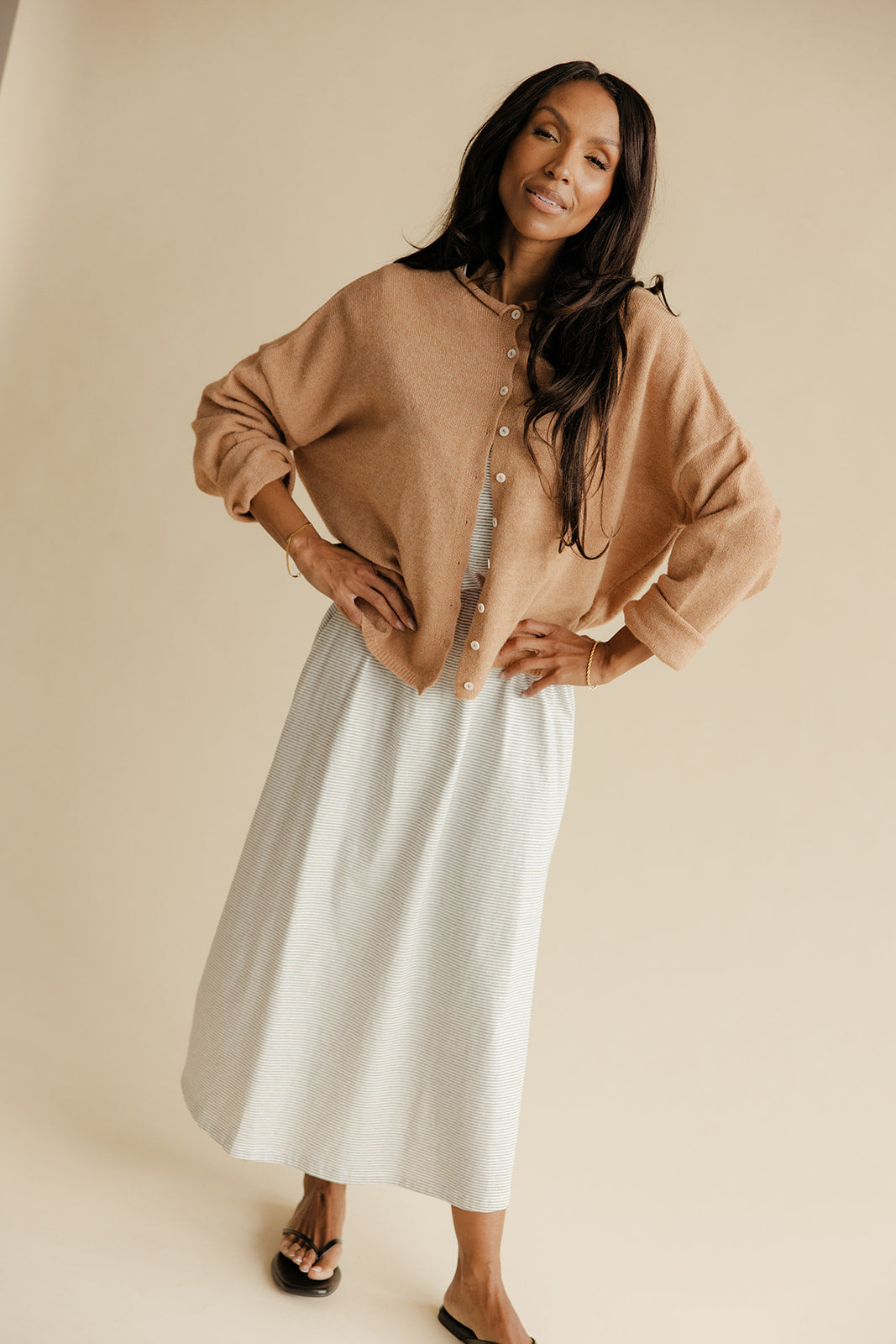 Woman wearing a beige sweater and light blue skirt against a beige background
