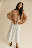 Woman wearing a beige sweater and light blue skirt against a beige background