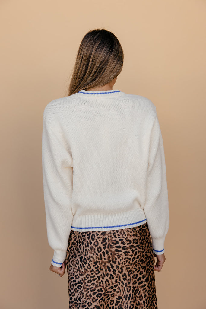 Person wearing a white sweater with a blue trim and a leopard print skirt on a beige background
