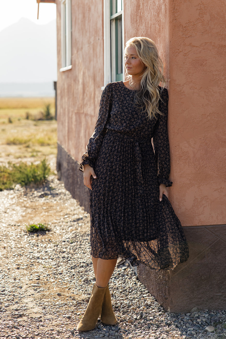 a woman in a dress leaning against a wall