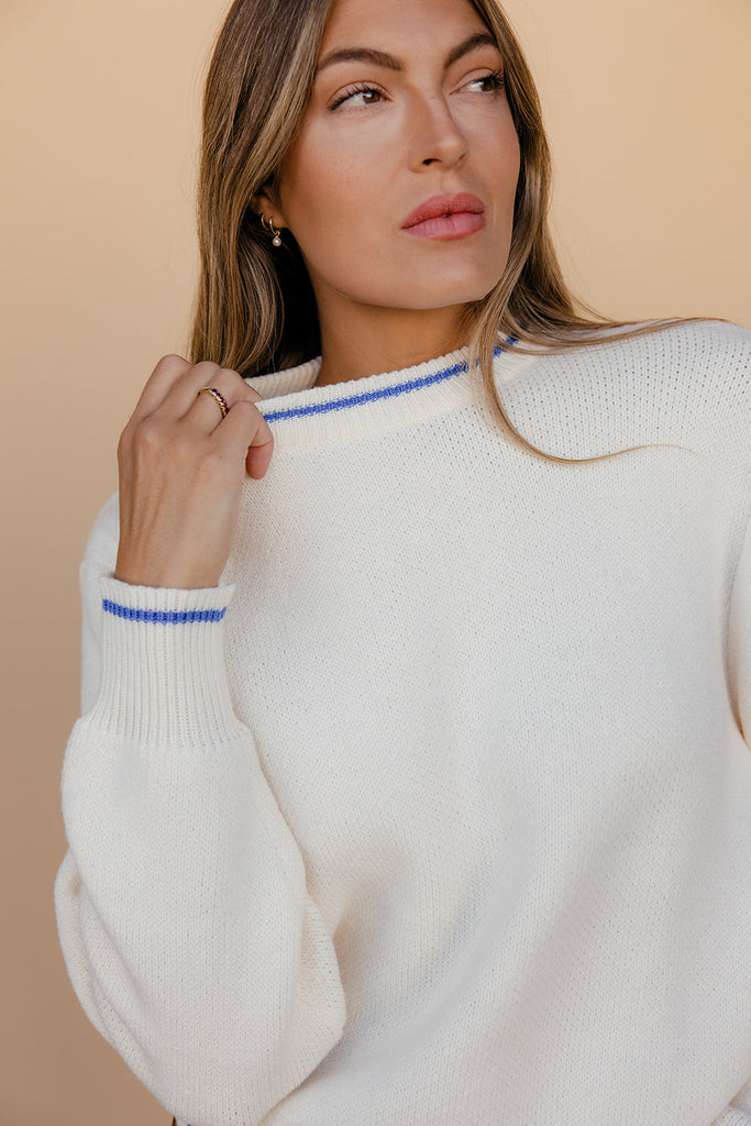 Woman wearing a white sweater with blue trim against a beige background