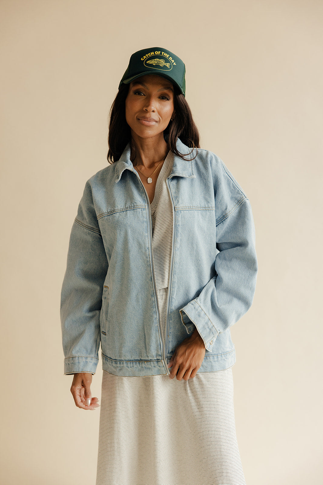 Woman wearing a denim jacket and cap against a beige background