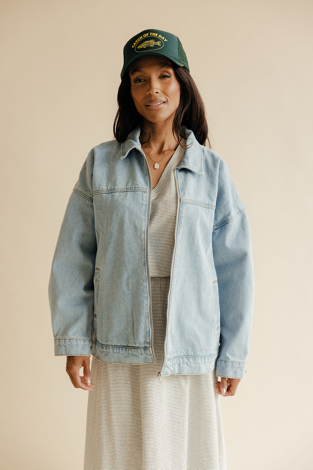 Woman wearing a denim jacket and green cap against a beige background