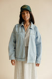 Woman wearing a denim jacket and green cap against a beige background