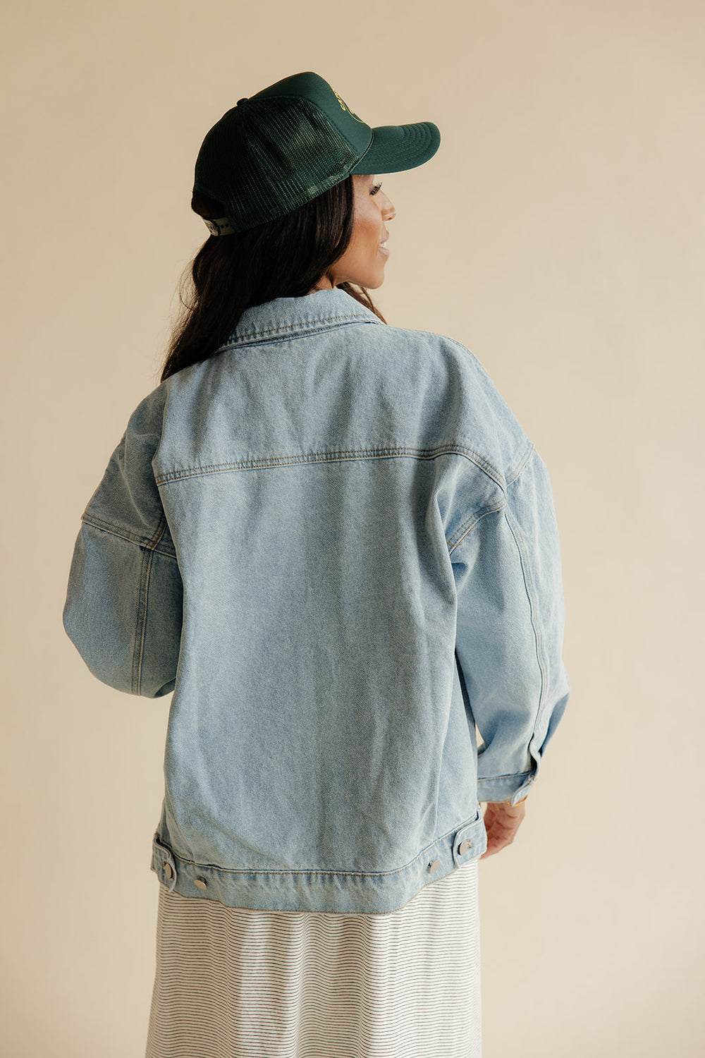 Person wearing a denim jacket and green cap on a beige background