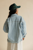 Person wearing a denim jacket and green cap on a beige background
