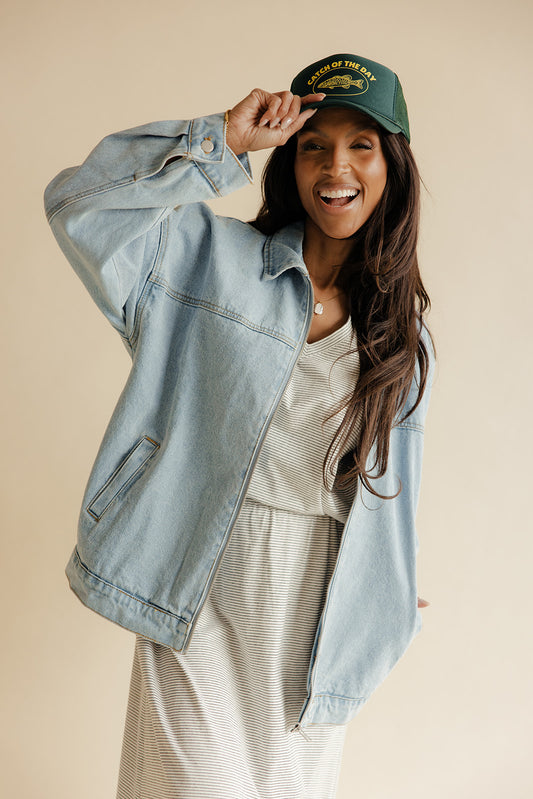 Woman wearing a denim jacket and green cap against a beige background