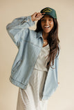 Woman wearing a denim jacket and green cap against a beige background