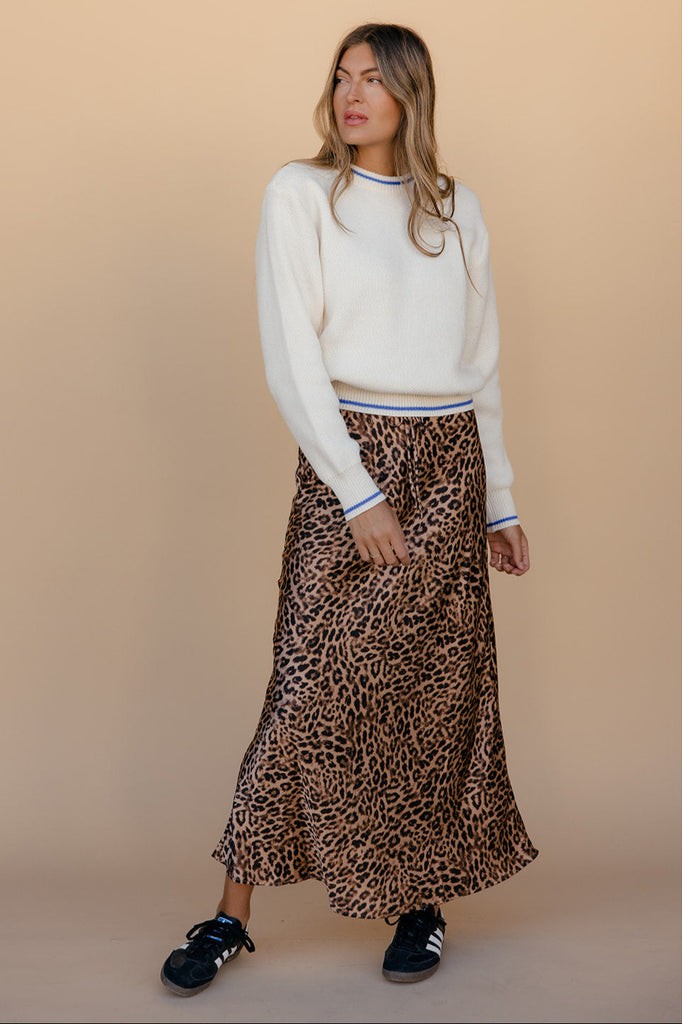 Woman wearing a white sweater and leopard print skirt against a beige background
