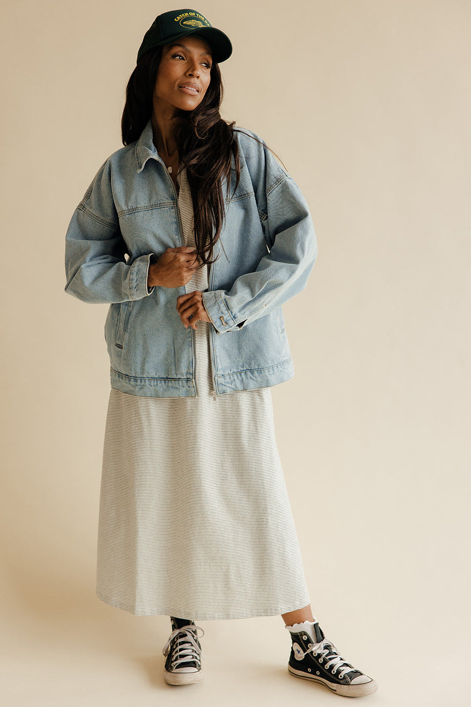 Person wearing a denim jacket, beige coat, and black sneakers on a beige background