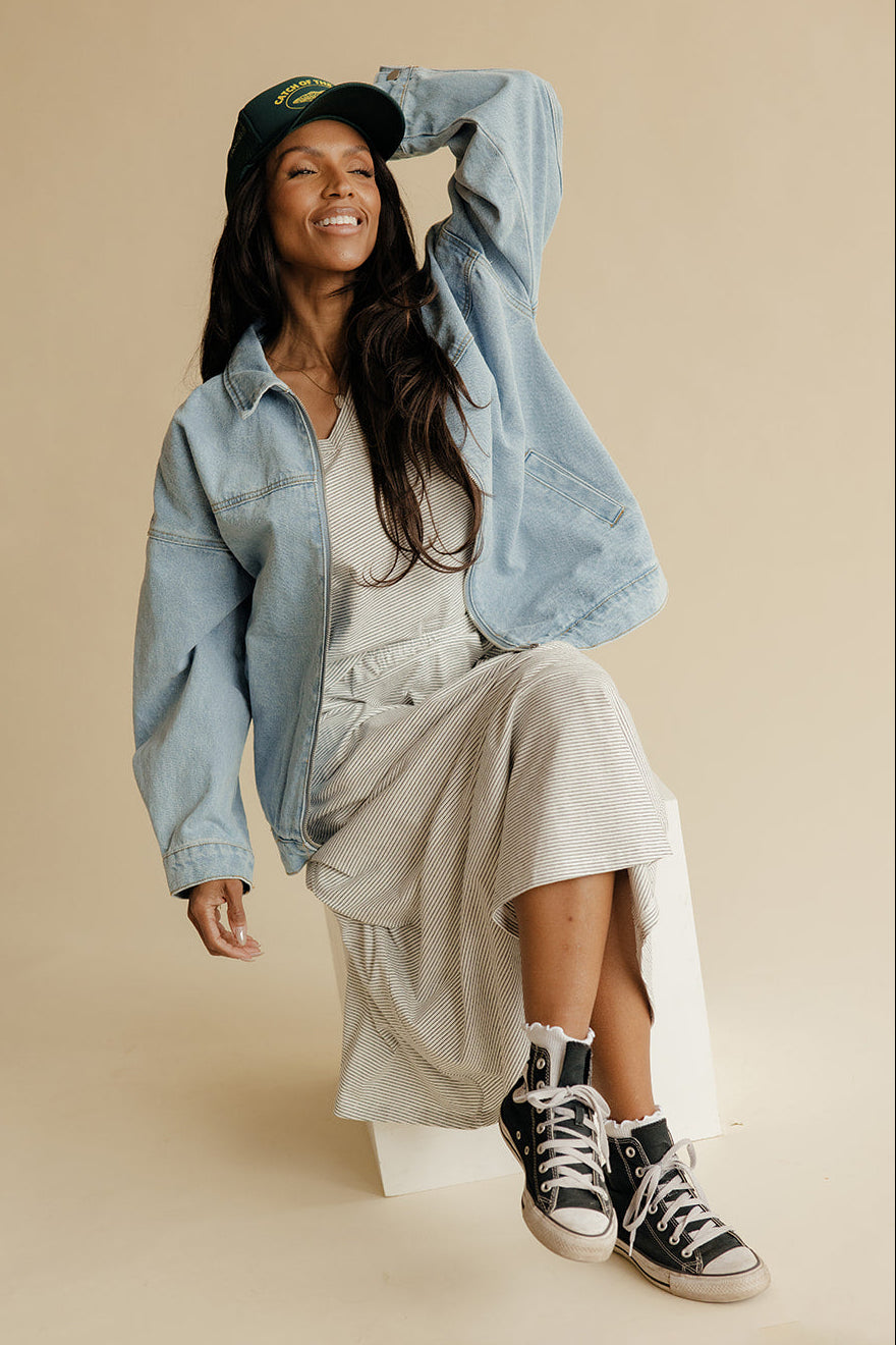 Woman wearing a denim jacket, beige dress, and black sneakers on a beige background