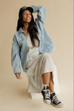Woman wearing a denim jacket, beige dress, and black sneakers on a beige background