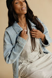 Woman wearing a denim jacket over a striped outfit on a beige background